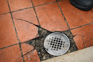 Cracked tile and deteriorating grout surrounding a commercial stainless steel floor drain