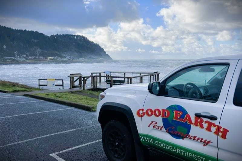 A Good Earth Pest Company route truck parked along the coast with ocean waves crashing in the background.