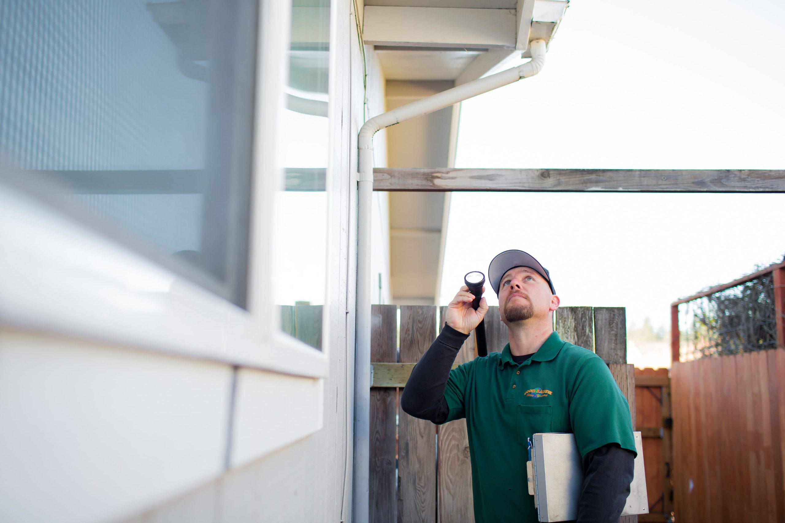 Good Earth Pest Company technician inspecting the exterior of a home with a flashlight.